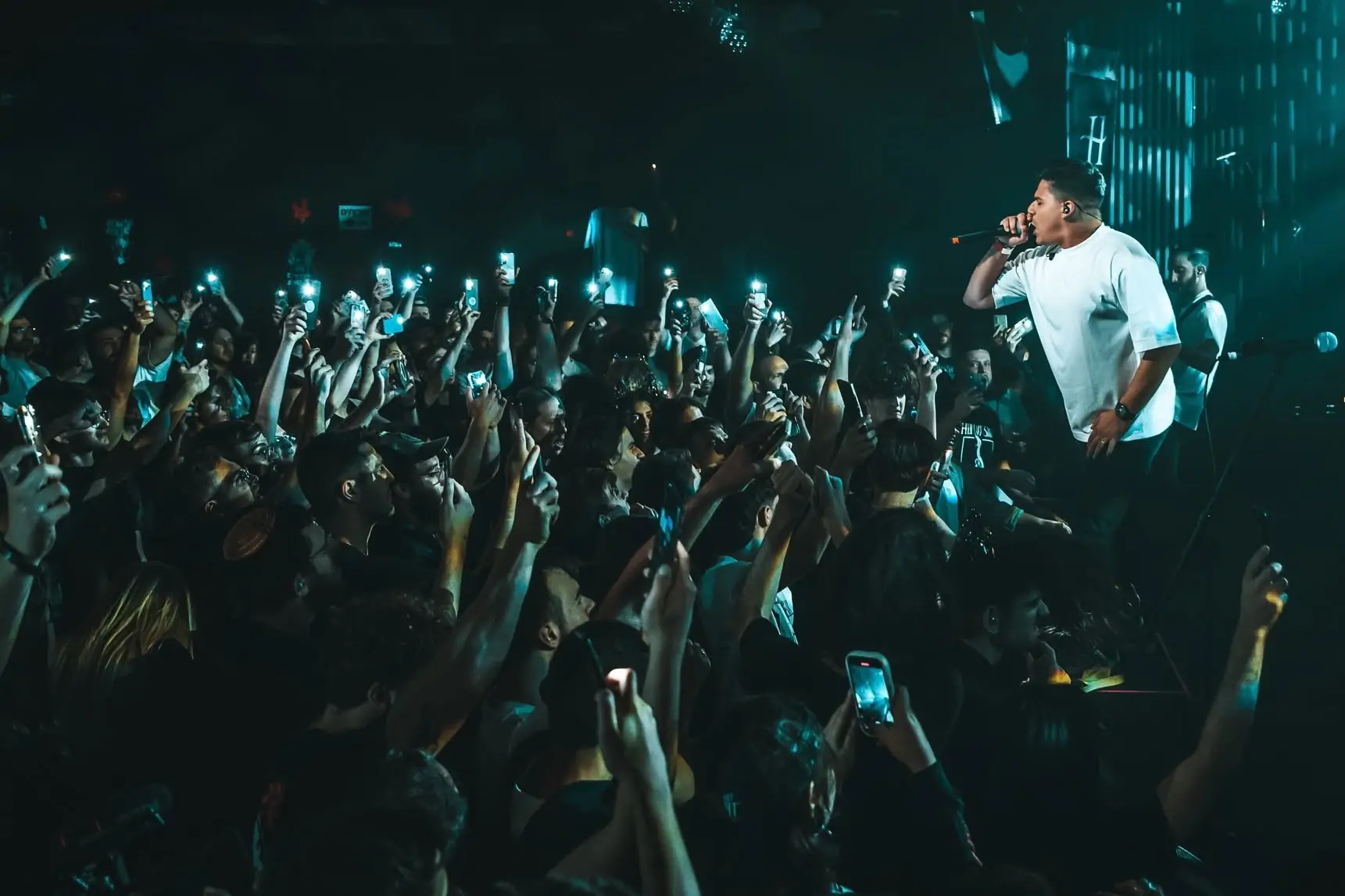 A singer in a white shirt on stage facing a crowd holding up lit phones