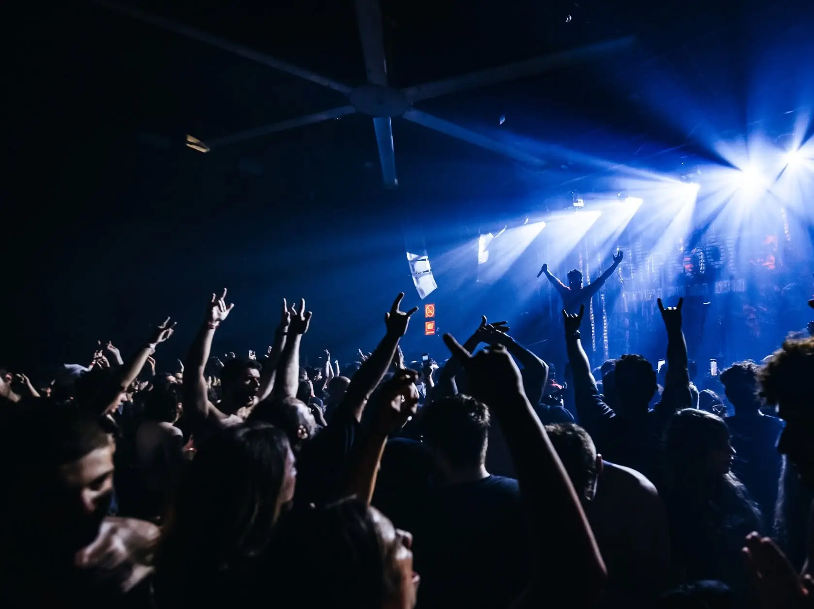 A crowd with raised hands facing a stage lit in blue