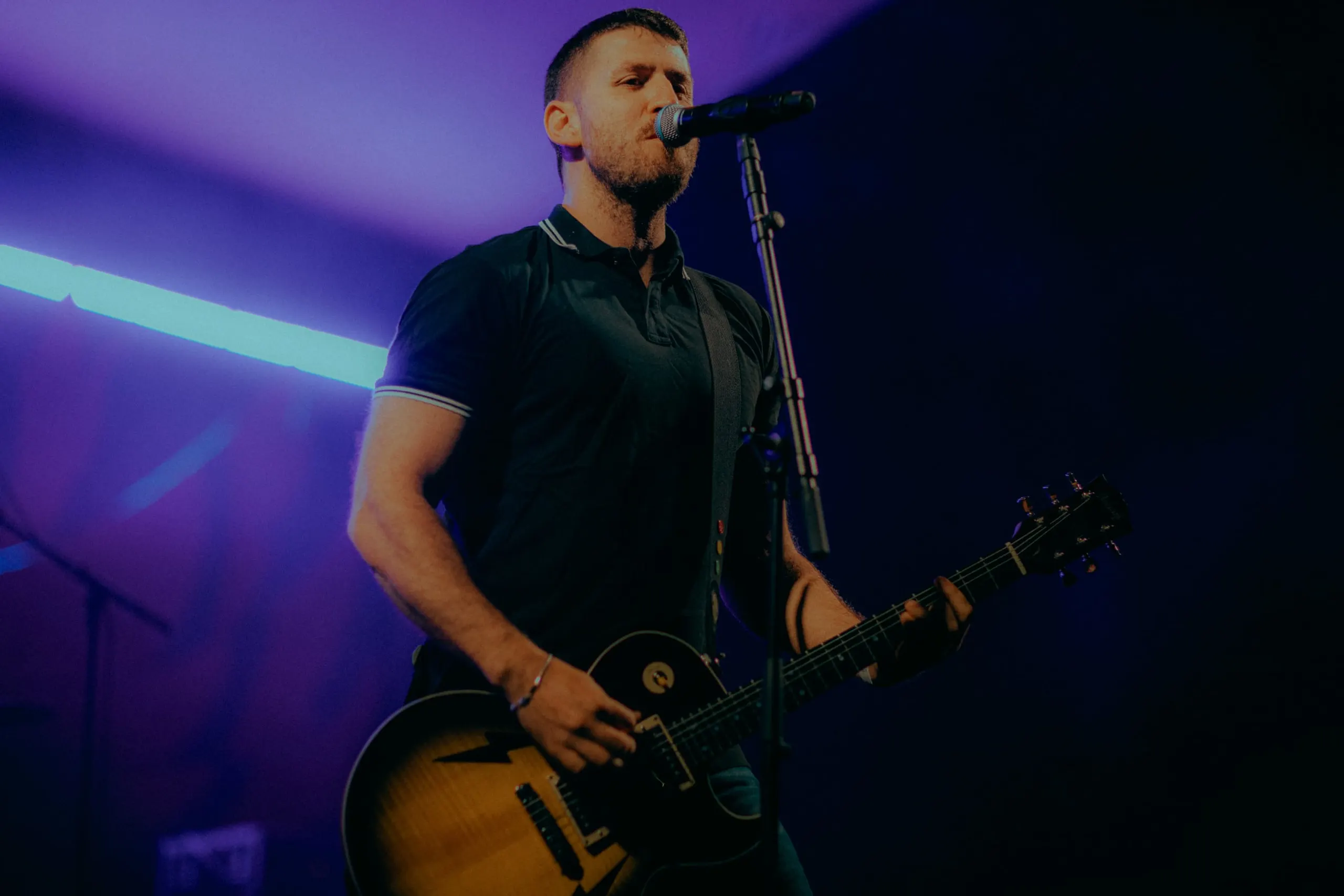 The City Revival's singer at the mic with a guitar, in purple light
